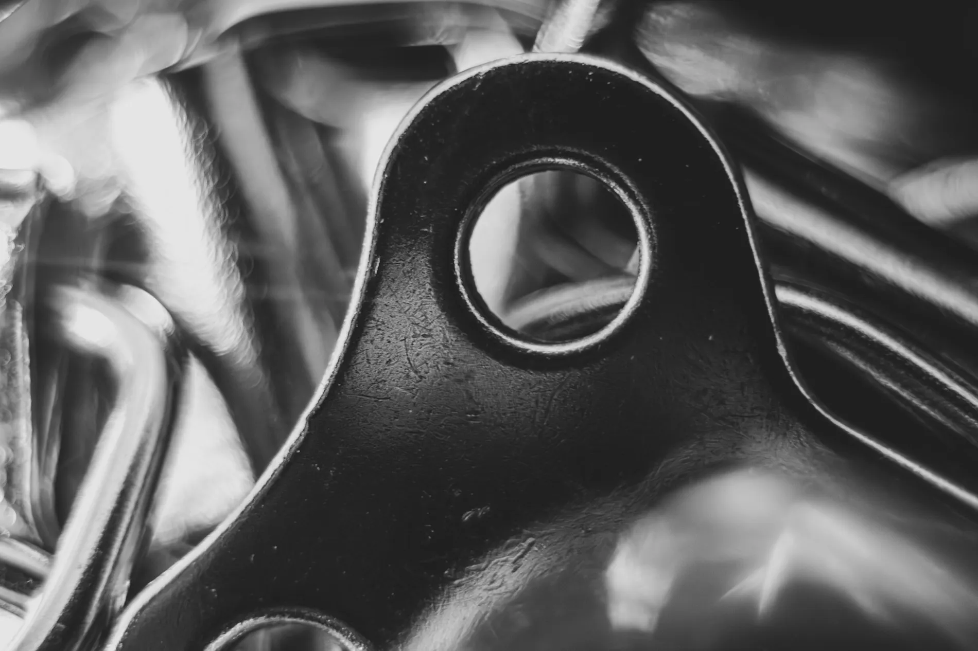 A machined bracket with a single bored hole, wet with oil, lit hard from one side.