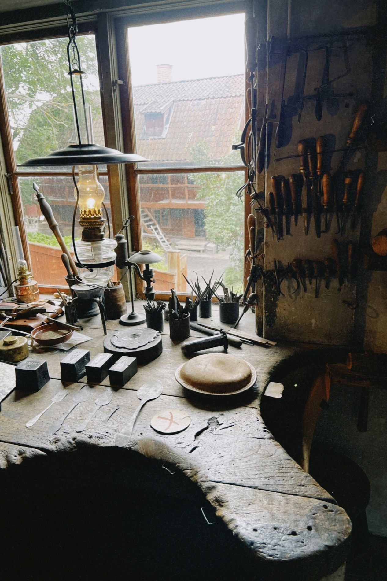 A workbench under a window, an oil lamp and hand tools laid out across the worn top