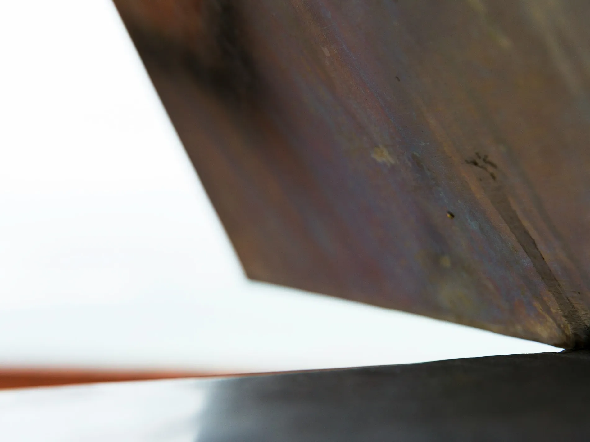 A torn sheet of white lying across a weathered metal plate, the two surfaces meeting on one hard diagonal.